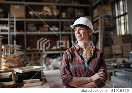 Portrait of mid-adult female carpenter standing in carpentery workshop, looking aside and smiling. Small business concept. Portrait of mid-adult female carpenter standing in carpentery workshop, looking aside and smiling. Small business concept. 81916850