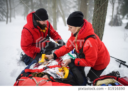 Mountain rescue service provide operation outdoors in winter in forest, injured person in stretcher. Mountain rescue service provide operation outdoors in winter in forest, injured person in stretcher. 81916890