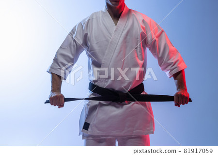 Cropped portrait of karate, judo sportsman in white kimono tying black belt isolated over gradient white blue background Cropped portrait of karate, judo sportsman in white kimono tying black belt isolated over gradient white blue background 81917059