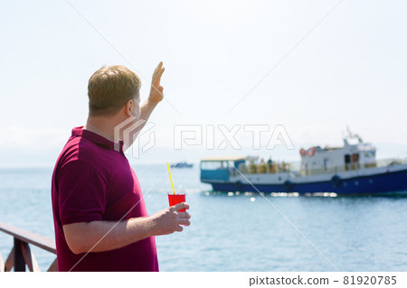 A man on a pier by the sea with a smile waves to a passing ship 81920785