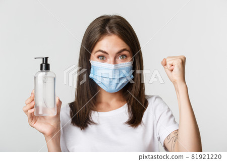 Covid-19, health and social distancing concept. Close-up of attractive smiling girl in medical mask, showing hand sanitizer, recommend antiseptic Covid-19, health and social distancing concept. Close-up of attractive smiling girl in medical mask, showing hand sanitizer, recommend antiseptic 81921220