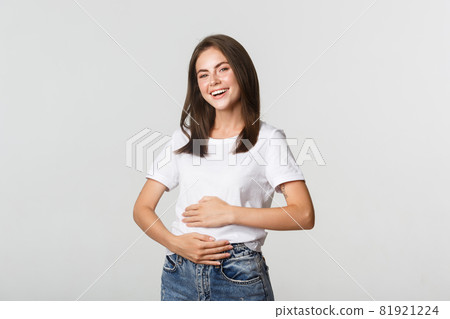 Satisfied smiling brunette girl rubbing belly after eating delicious food Satisfied smiling brunette girl rubbing belly after eating delicious food 81921224