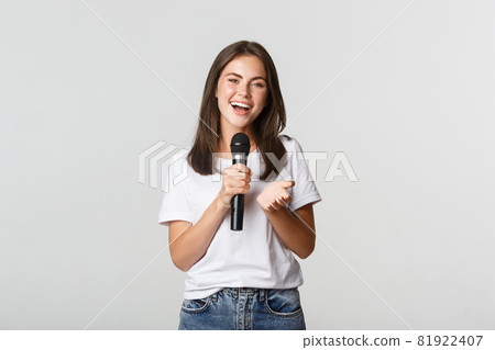 Beautiful young woman singing song in microphone at karaoke, standing white background 81922407