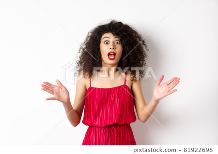 Excited woman with curly hair, talking with amazed face, explain big news, shaking hands and look astonished at camera, white background Excited woman with curly hair, talking with amazed face, explain big news, shaking hands and look astonished at camera, white background 81922698