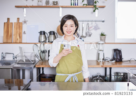 一位穿著圍裙的年輕女子在廚房裡操作智能手機 一位穿著圍裙的年輕女子在廚房裡操作智能手機 81923133