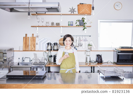 一位穿著圍裙的年輕女子在廚房裡操作智能手機 81923136