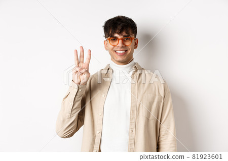 Handsome caucasian guy in glasses showing three fingers and smiling, standing on white background Handsome caucasian guy in glasses showing three fingers and smiling, standing on white background 81923601