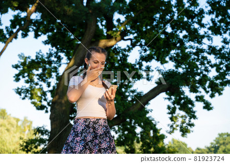Girl phone. Euphoric screaming young girl holding smartphone showing winner gesture at sunny day in park. Messaging, being happy to text. Girl phone. Euphoric screaming young girl holding smartphone showing winner gesture at sunny day in park. Messaging, being happy to text. 81923724