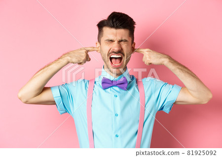 Irritated young man block noise, shut ears with hands and screaming annoyed, being disturbed by loud sound, standing over pink background 81925092