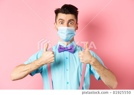 Coronavirus, healthcare and quarantine concept. Satisfied guy in medical mask showing thumbs up in approval, praising excellent choice, pink background 81925550
