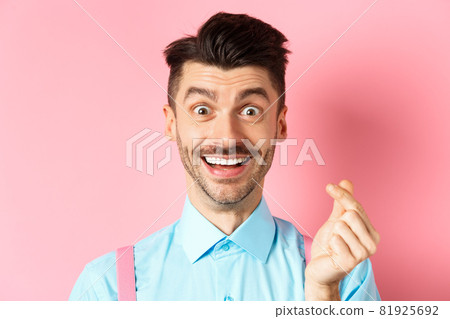 Valentines day concept. Smiling man showing finger heart and looking happy, standing over pink background Valentines day concept. Smiling man showing finger heart and looking happy, standing over pink background 81925692