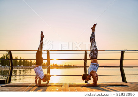 Couple practicing acrobatic yoga together, doing Handstand pose on nature outdoors at sea. 81928090