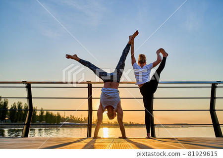 Couple practicing acrobatic handstand yoga together on nature outdoors at sea. Couple practicing acrobatic handstand yoga together on nature outdoors at sea. 81929615