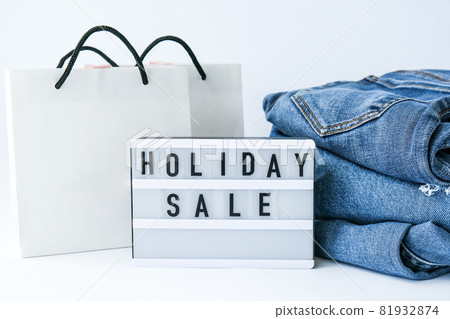 Light board with text HOLIDAY SALE with paper shopping bags, jeans clothes. Big Sale online shopping concept. Promotion advertising. Holiday Light board with text HOLIDAY SALE with paper shopping bags, jeans clothes. Big Sale online shopping concept. Promotion advertising. Holiday 81932874