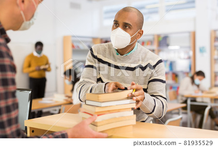 Man in mask returning books at library 81935529