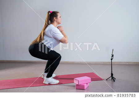 A chubby young woman is watching an online fitness lesson on a mobile phone. Distance sports training 81935783