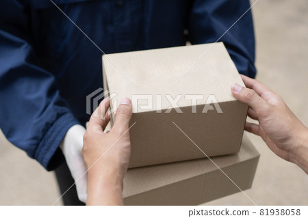 Parcel delivery concept the postman in white rubber gloves and light weight dark blue coat handing two small parcel posts to his client 81938058