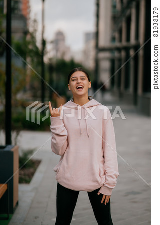 Playful portrait of pretty young woman, having fun at the street. 81938179