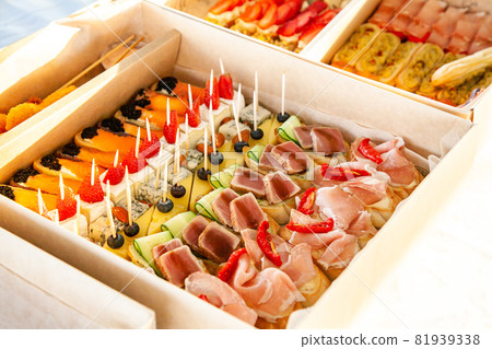 Gourmet snacks in cardboard box with sandwiches, eclairs, bruschetta with cold cuts, cheese and seafood for catering buffet and party. 81939338