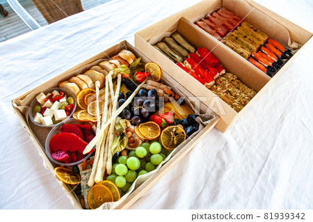 Delicious wine snacks in a cardboard box for a buffet for a party: cheeses, sausages, cold cuts, fruit, baguette, Grissini 81939342