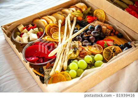 Delicious wine snacks in a cardboard box for a buffet for a party: cheeses, sausages, cold cuts, fruit, baguette, Grissini 81939416