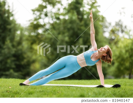 Happy smiling young woman in sportswear standing in Side Plank Vasisthasana pose outside in nature Happy smiling young woman in sportswear standing in Side Plank Vasisthasana pose outside in nature 81940147