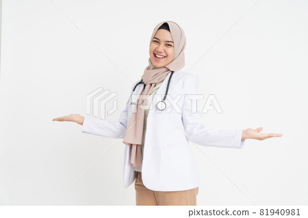 smiling female doctor in headscarf with offering gesture with two hands looking at the camera smiling female doctor in headscarf with offering gesture with two hands looking at the camera 81940981