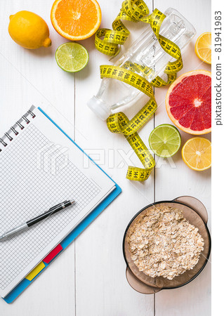 Healthy breakfast with oatmeal, fresh fruits and bottle of water with notebook on rustic wooden table. 81941983