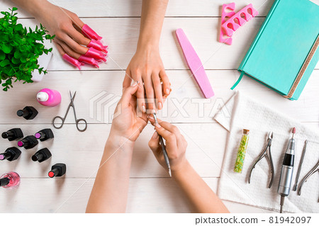 Manicure for the client. Close-up of the hands of a manicurist and client on a wooden background Manicure for the client. Close-up of the hands of a manicurist and client on a wooden background 81942097