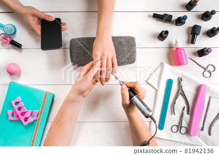 Manicure for the client. Close-up of the hands of a manicurist and client on a wooden background Manicure for the client. Close-up of the hands of a manicurist and client on a wooden background 81942136