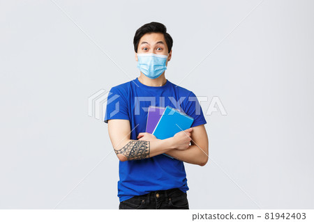 Back to school, studying during covid-19, education and university life concept. Excited happy young male asian student in medical mask heading campus, smiling and holding notebooks 81942403
