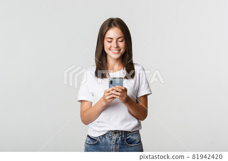 Smiling attractive girl using mobile phone and looking at screen pleased Smiling attractive girl using mobile phone and looking at screen pleased 81942420