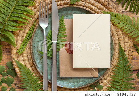 Blank paper card and envelope on table setting with fern leaves on wooden table Blank paper card and envelope on table setting with fern leaves on wooden table 81942458
