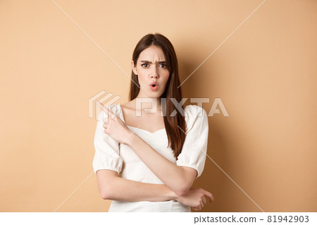 What is that. Shocked and angry woman scolding person, frowning and pointing left with confused face, waiting for explanation, standing on beige background 81942903