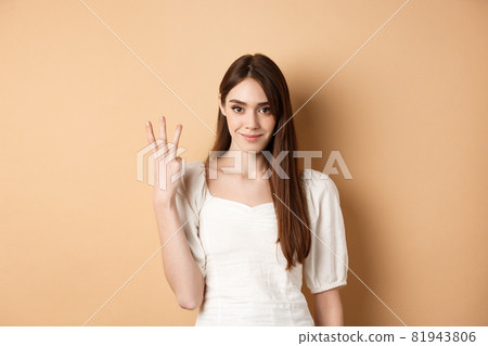 Attractive young woman show fingers number three, smiling and looking confident, standing on beige background Attractive young woman show fingers number three, smiling and looking confident, standing on beige background 81943806