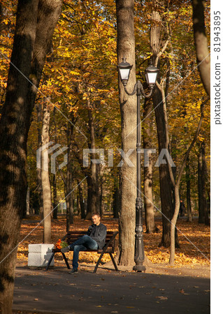Sad man is sitting on a bench in an autumn city park with a bouquet of flowers and waits for a long time with a dissatisfied expression on his face. A failed date Sad man is sitting on a bench in an autumn city park with a bouquet of flowers and waits for a long time with a dissatisfied expression on his face. A failed date 81943895