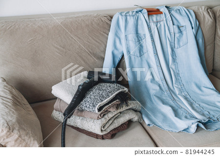 A stack of clean warm clothes and shirt with a steam cleaner on A stack of clean warm clothes and shirt with a steam cleaner on 81944245