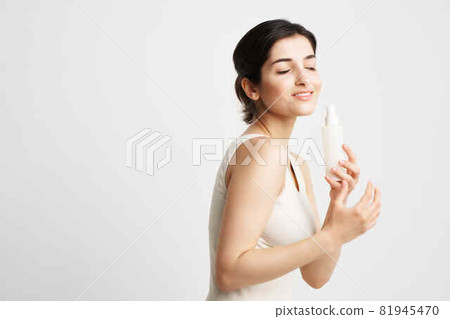 brunette in a white tank top with lotion in her hands clean skin 81945470
