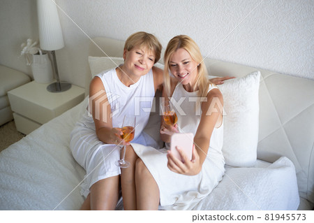 woman with mom drinking wine sitting on bed and taking a selfie woman with mom drinking wine sitting on bed and taking a selfie 81945573