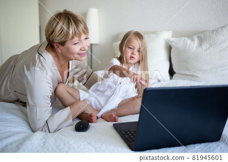 little girl with her grandmother sitting on the bed in front of a laptop little girl with her grandmother sitting on the bed in front of a laptop 81945601