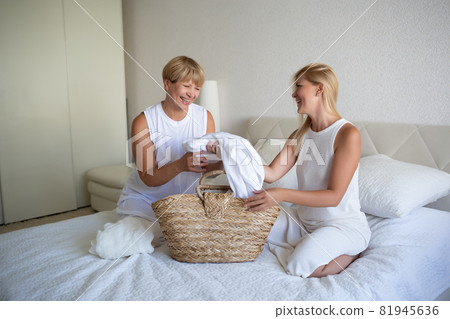 woman with mom disassemble the laundry while sitting on the bed in the bedroom woman with mom disassemble the laundry while sitting on the bed in the bedroom 81945636