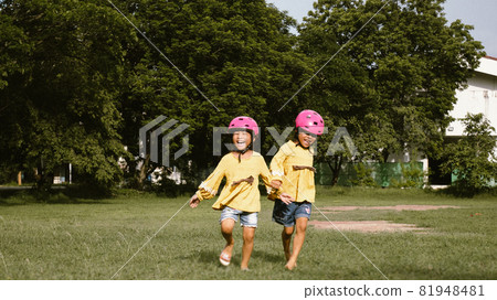 Two cute little sisters in helmet running on the lawn in park on a sunny summer day, taking a break after cycling practice. Happy childhood. Family spending time together. Two cute little sisters in helmet running on the lawn in park on a sunny summer day, taking a break after cycling practice. Happy childhood. Family spending time together. 81948481