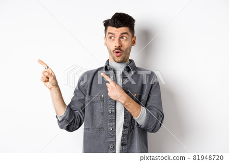 Stylish guy say wow, pointing and looking left with excited face, showing banner logo, standing on white background Stylish guy say wow, pointing and looking left with excited face, showing banner logo, standing on white background 81948720