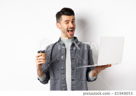 Happy male worker drinking coffee and work with laptop, winking at camera, standing on white background Happy male worker drinking coffee and work with laptop, winking at camera, standing on white background 81949053