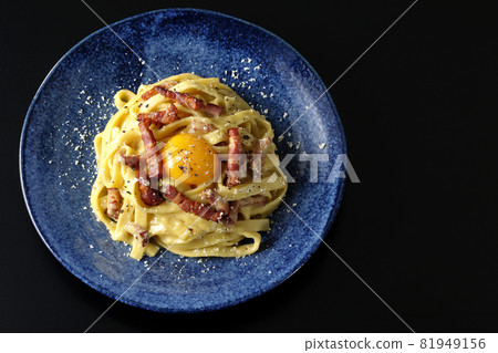 A bird's-eye view of Fettuccine's carbonara with egg yolk and crispy bacon on a black background 81949156