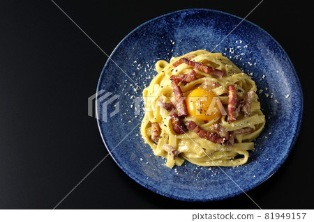 A bird's-eye view of Fettuccine's carbonara with egg yolk and crispy bacon on a black background A bird's-eye view of Fettuccine's carbonara with egg yolk and crispy bacon on a black background 81949157