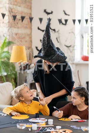 Cute boy with paintbrush looking at teacher in witch hat 81951521
