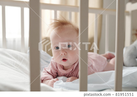 Cute infant girl in pink clothes crowling in her cradle 81951551