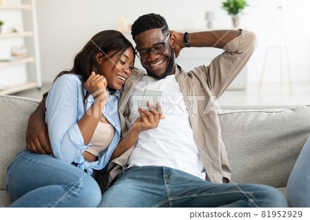 African american couple sitting on couch, using cellphone African american couple sitting on couch, using cellphone 81952929
