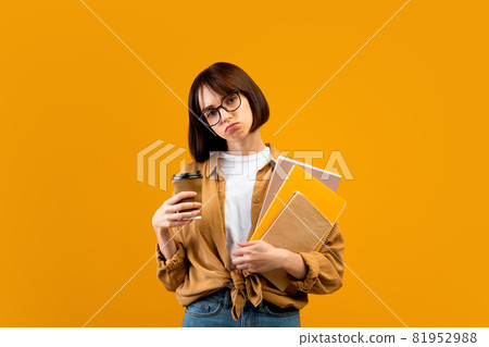 So tired. Exhausted female student with notebooks and takeaway coffee looking at camera on yellow background 81952988